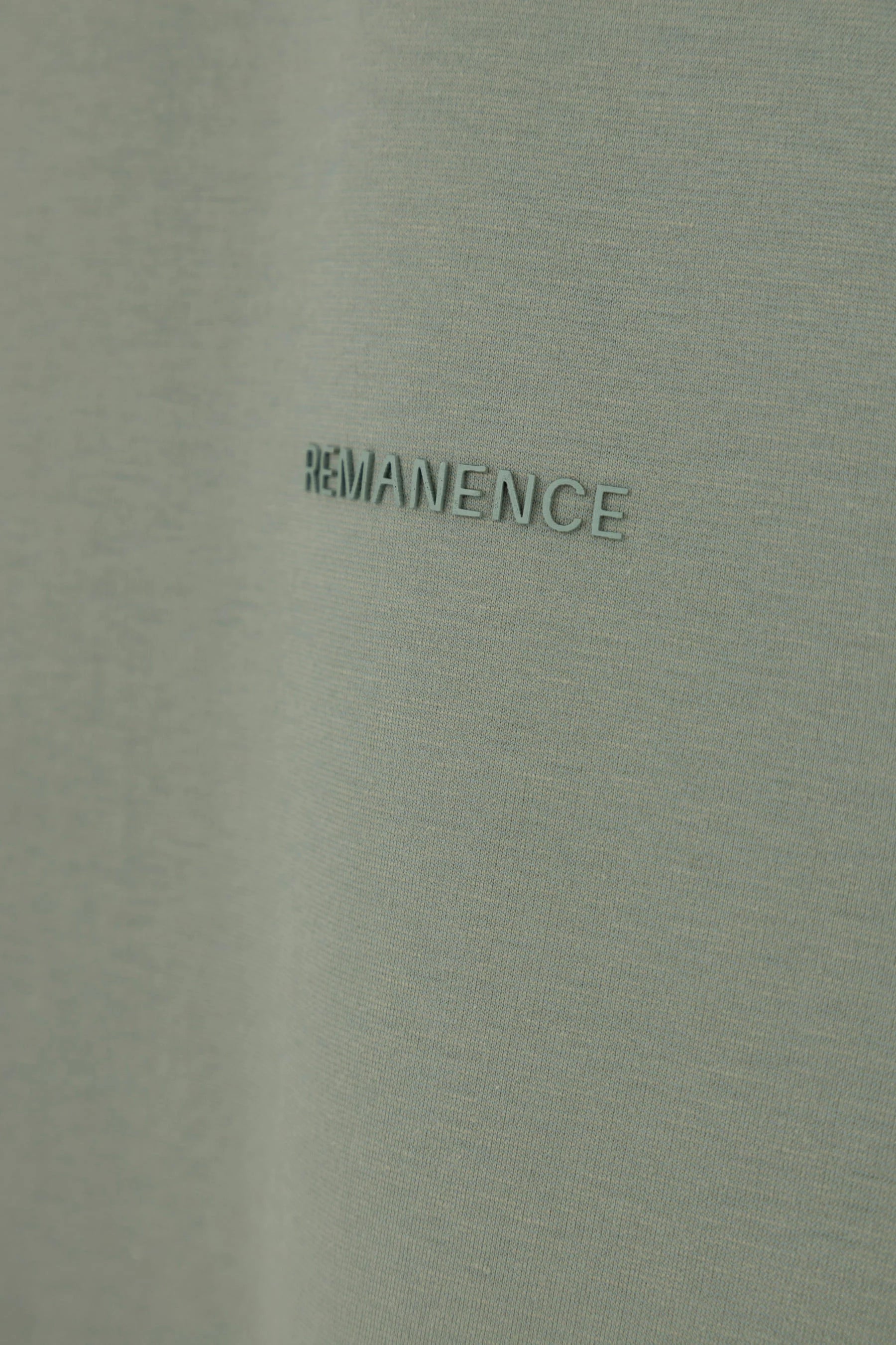 Detalle del logo Remanence en camiseta verde grisáceo semi fitted para hombre.