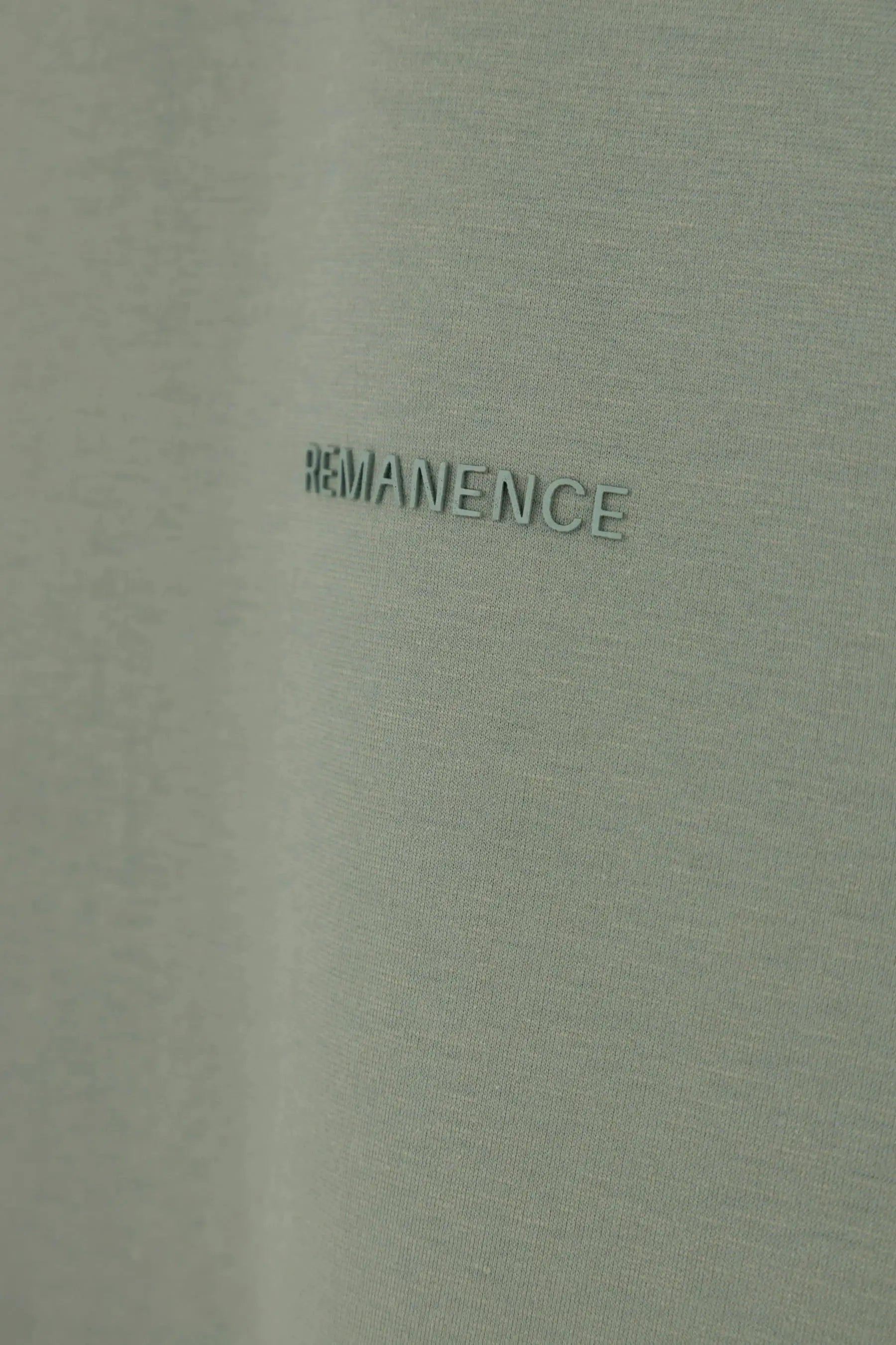 Detalle del logo Remanence en camiseta verde grisáceo semi fitted para hombre.