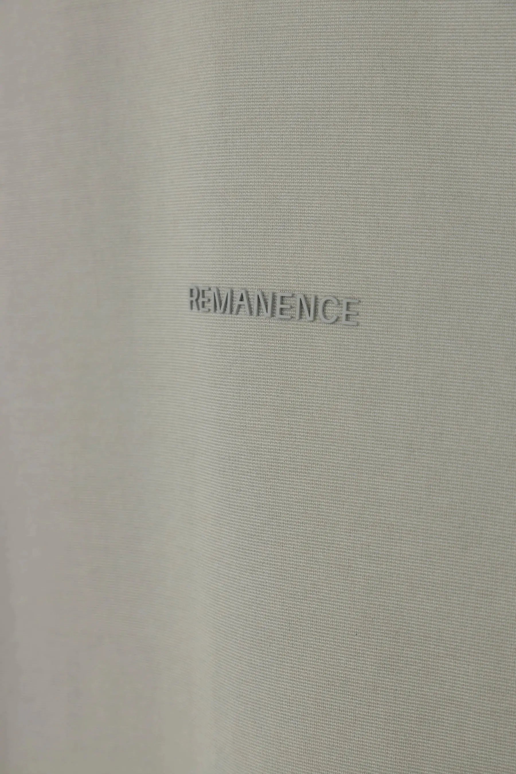 Detalle del logo Remanence en camiseta gris claro semi fitted para hombre.