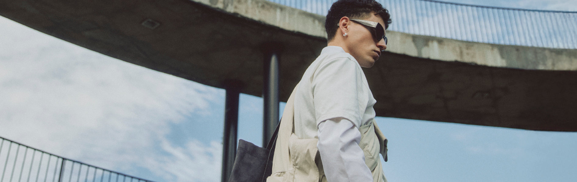 Hombre con t-shirt blanca y chaqueta Remanence, estilo techwear urbano en entorno arquitectónico moderno.