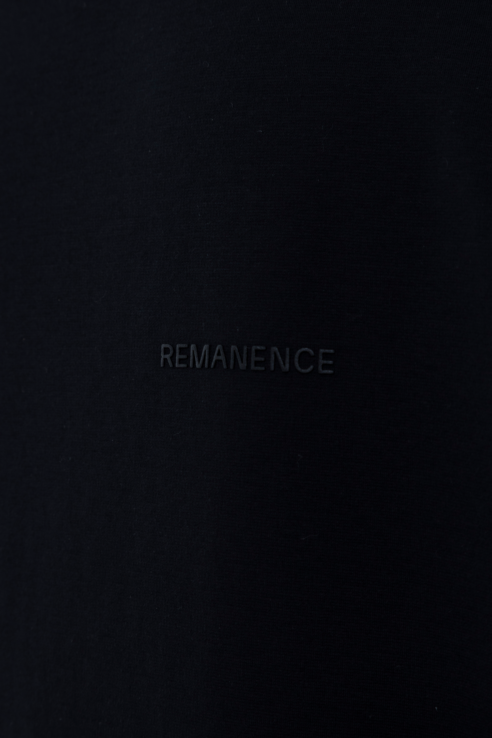 Detalle del logo Remanence en relieve sobre camiseta negra slim fit hombre